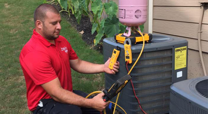 Technician in red polo shirt, testing an outdoor AC unit.